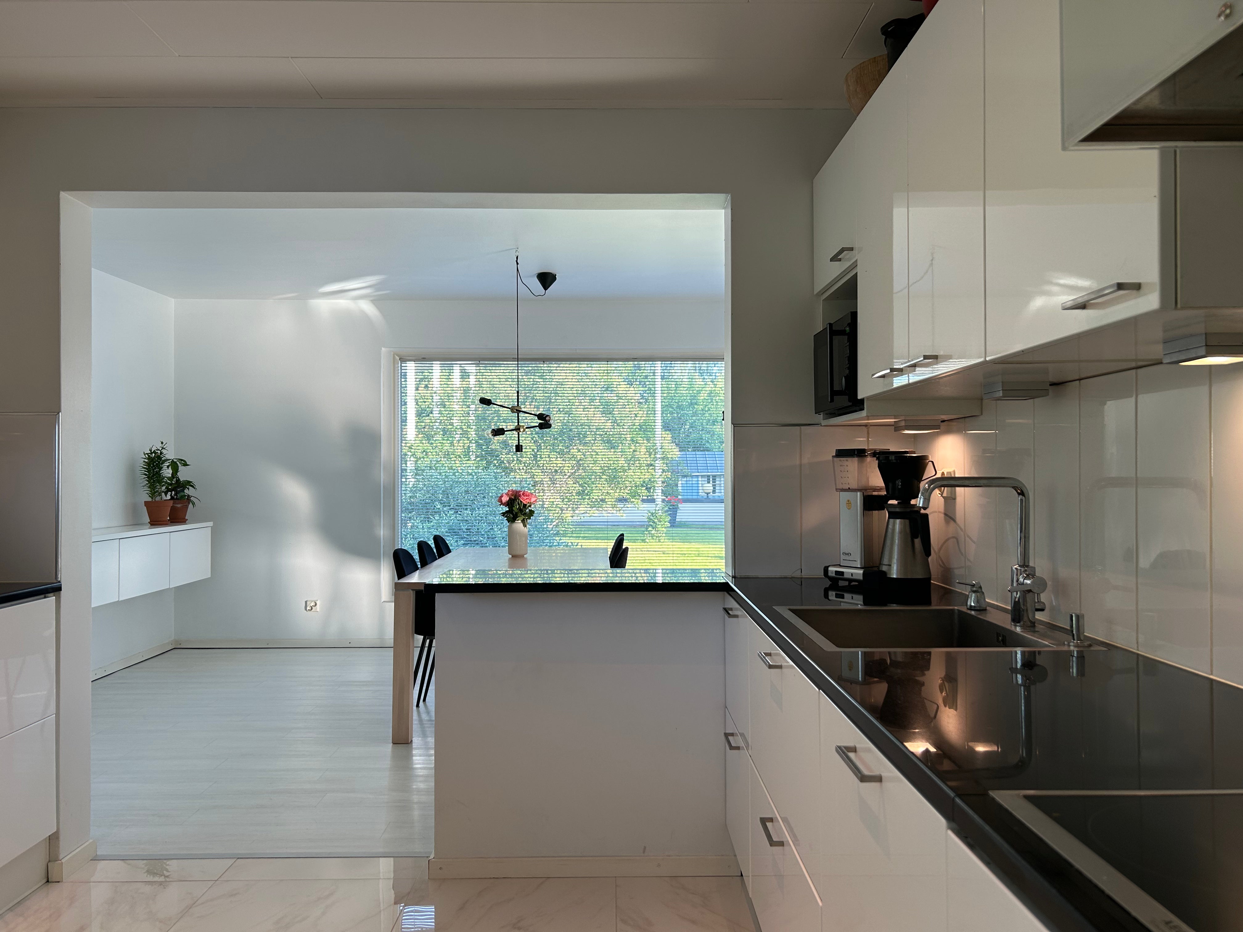 Modern kitchen with black countertops and white cabinets, featuring a window view of greenery. Arctic Lapland Villa