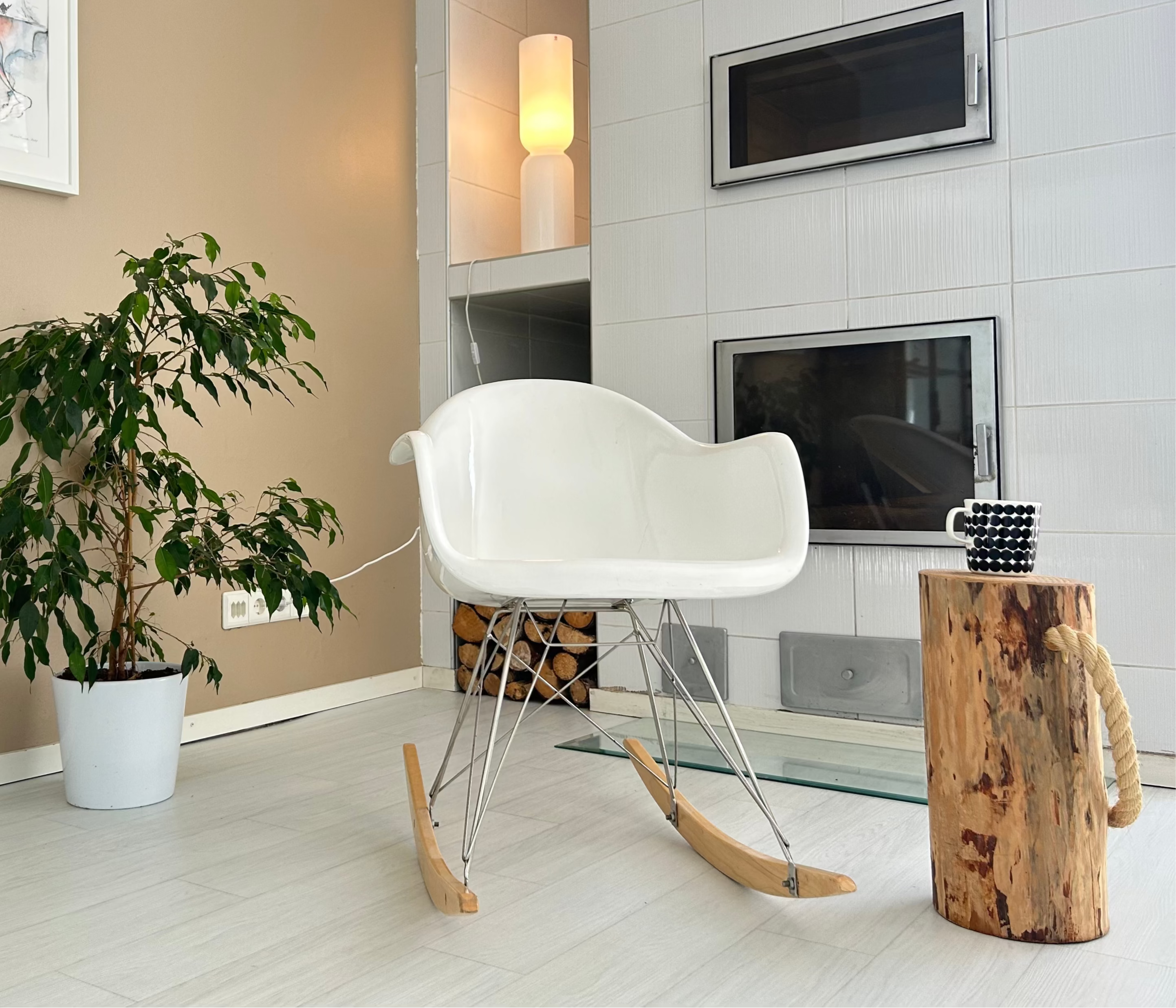 Modern living room with a white chair, plant, and wooden side table. Villa in Lapland.