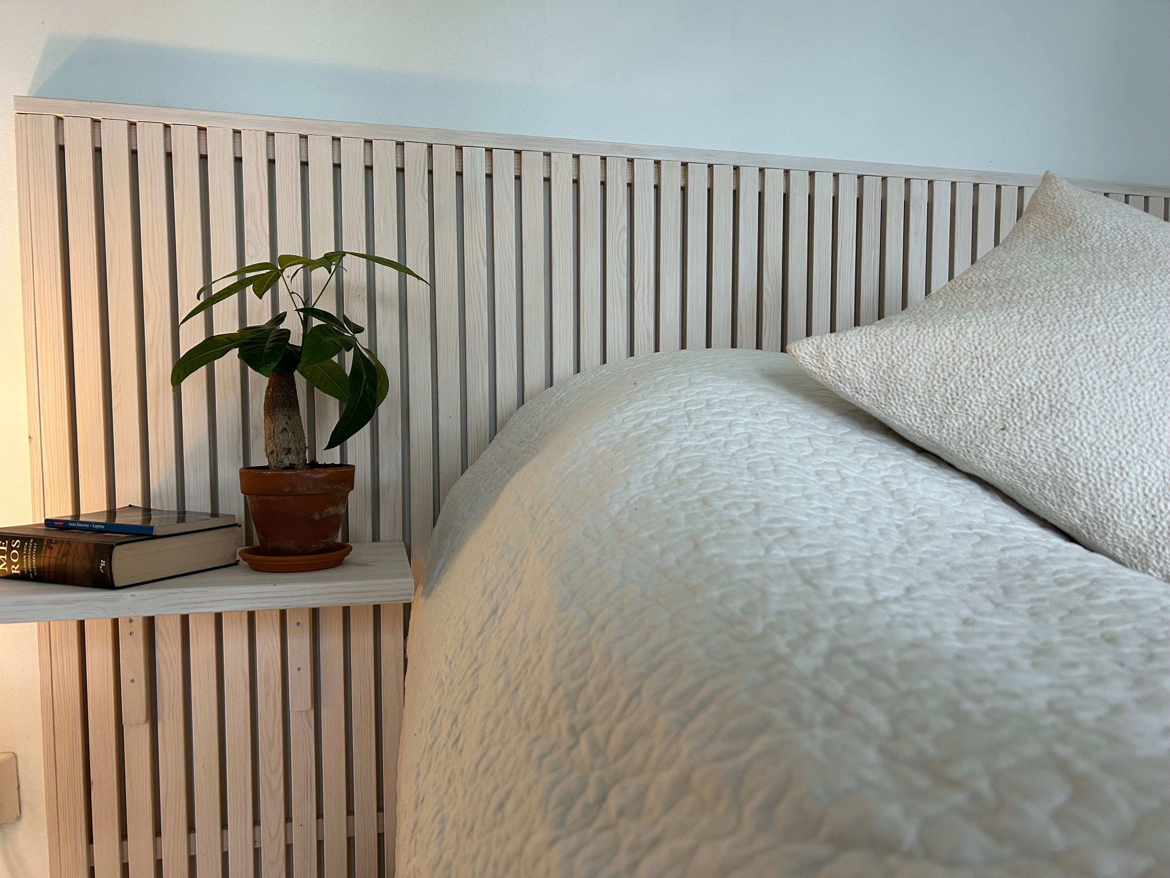 Bed with wooden headboard and nightstand featuring a plant and books. Villa in Lapland